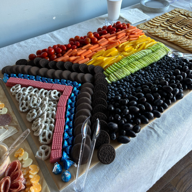 A charcuterie board that is put together to replicate the pattern of the Progress flag.